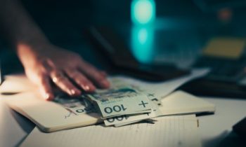 Close-up of hand reaching for banknotes on an office desk with a notebook and calculator.